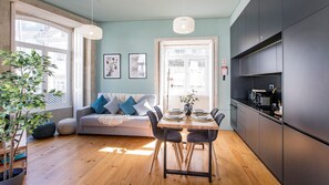 A modern kitchen with dark cabinets, a dining table set for four, and a sofa with blue cushions.