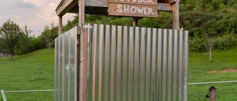 Une douche extérieure rustique, abritée par une structure et surmontée d’une enseigne en bois.