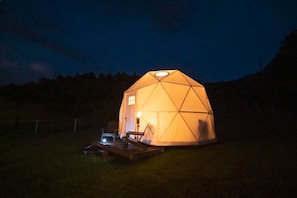 A geodesic dome tent with a small deck and a single light source inside. - Dome 1@ Smoky Mountains Glamping Dome #1 Read Details (Sevierville)
