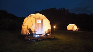 Zwei kuppelartige Jurten mit Tür und Fenstern, jede mit einer kleinen Veranda und Sitzgelegenheit.