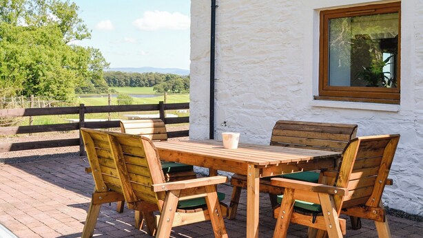 A wooden table and chairs on a patio with a white wall and window. - The Byre @ Camp Douglas (Castle Douglas)