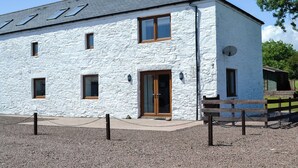 A white stone building with a grey roof, a wooden door, and multiple windows. - The Byre @ Camp Douglas (Castle Douglas)