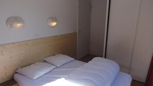 Un dormitorio con cabecera de madera, una cama con ropa blanca y dos lámparas fijadas a la pared.