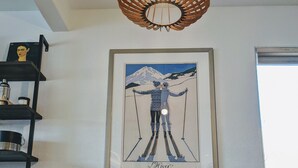 Ein Essbereich mit gerahmtem Kunstwerk, einer Pendelleuchte und einem Tisch mit Stühlen.