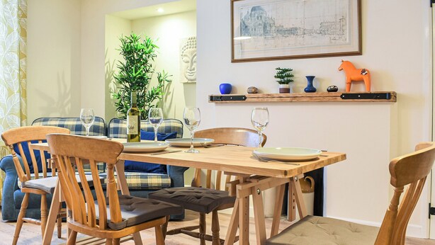 Un comedor con sillas de madera y una mesa dispuesta para cuatro personas. Hay una planta, una estatua de Buda y un estante con objetos decorativos.