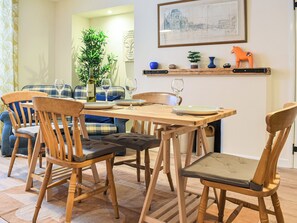 Un comedor con sillas de madera y una mesa dispuesta para cuatro personas. Hay una planta, una estatua de Buda y un estante con objetos decorativos.