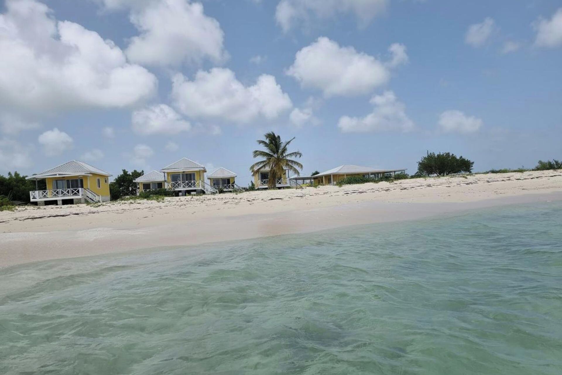 A beachfront property with multiple buildings, a sandy beach, and clear turquoise water.
