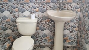 Bany amb vàter i rentapans, tots dos de color blanc, davant d'una paret amb mosaic de petxines.