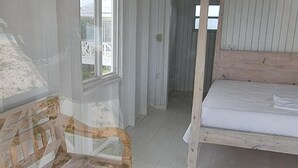 Un dormitori amb un llit de fusta, una finestra i una porta que dóna a una altra habitació.