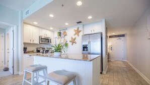 Une cuisine moderne avec des meubles blancs, un grand îlot central doté de tabourets, des appareils en acier inoxydable et des étoiles de mer décoratives accrochées au mur.