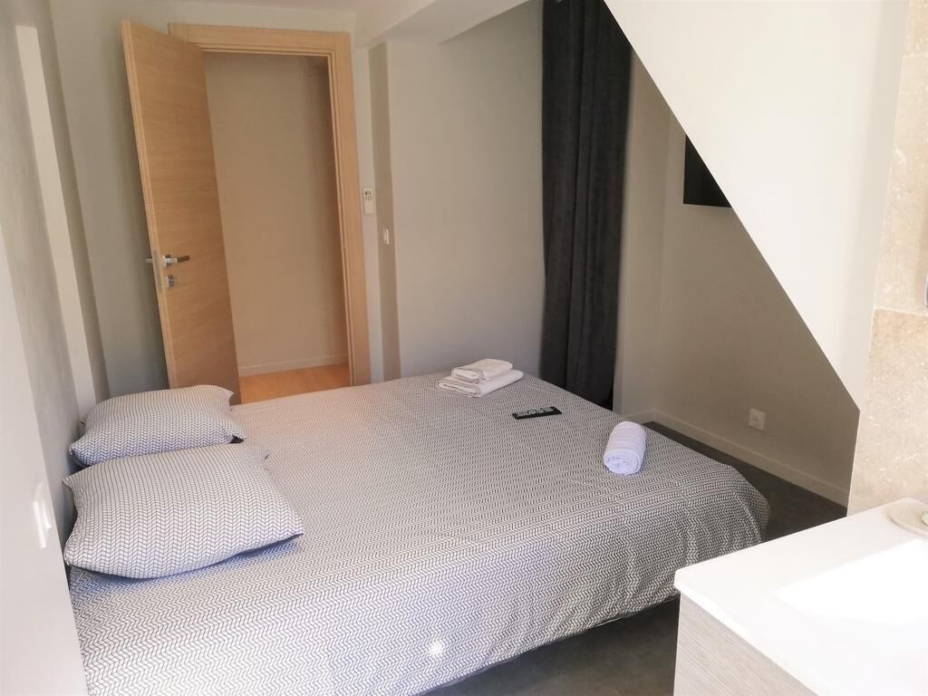 A small, neatly made bedroom with a bed, pillows, a folded towel, and a remote control.