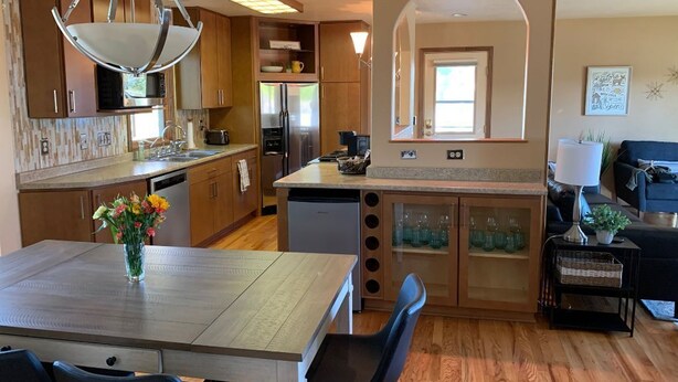 A modern kitchen with wooden cabinets, a central island, and a dining area with a table and chairs.