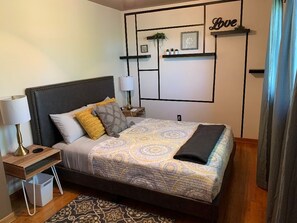 Un dormitorio ordenado con cama, mesita de noche, lámpara y paneles decorativos en la pared.