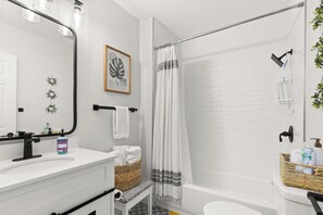 Een moderne badkamer met een wit wastafelmeubel, spiegel en douchegordijn. Handdoeken en toiletartikelen liggen op het aanrecht.