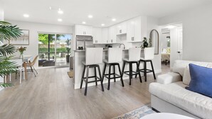 Una cocina moderna con armarios blancos, una isla central con taburetes y un área de comedor con mesa y sillas.