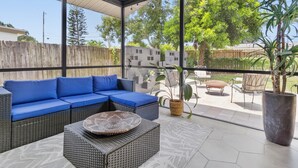 Un patio exterior techado con un sofá azul modular, mobiliario de mimbre y una planta grande en maceta.