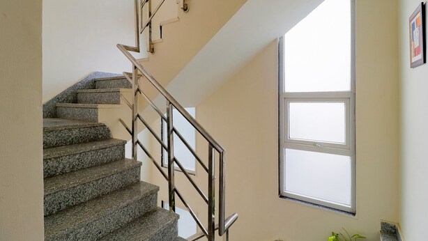 A staircase with granite steps and metal railings, leading to a landing with a large window. - Treebo Rejoice 52 - 3km From Huda City Metro Station (Gurugram)