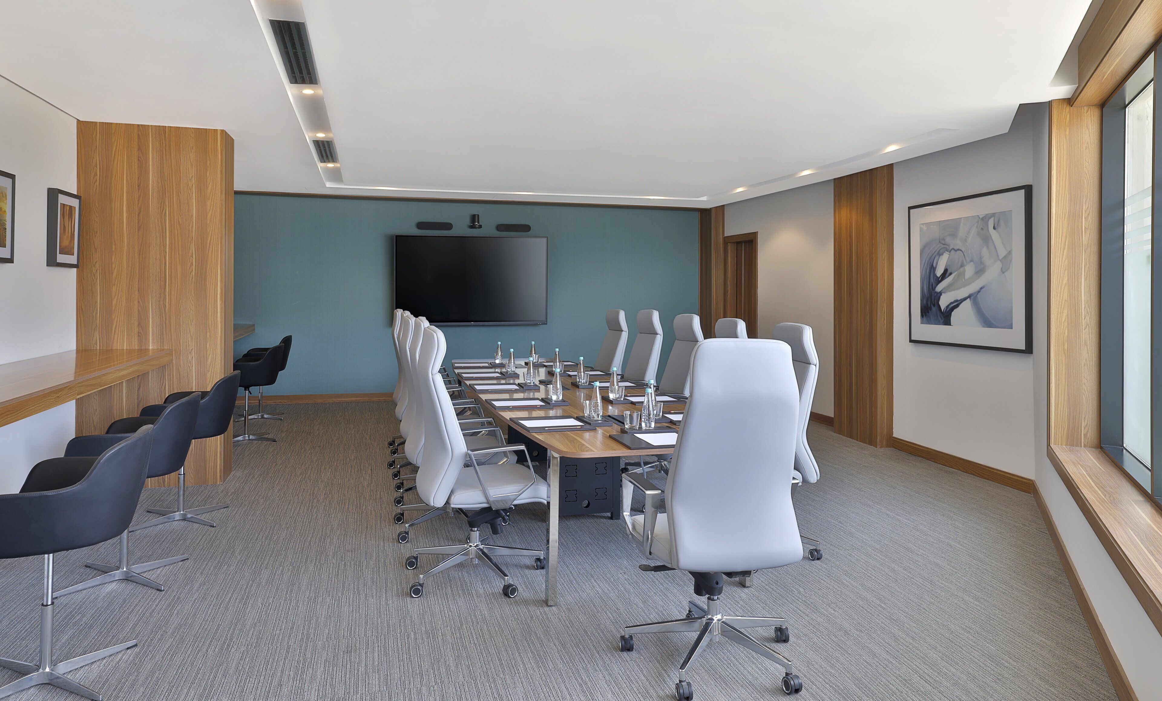 A conference room with a long table, white chairs, a flat-screen TV, and wooden paneling.