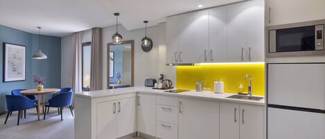 Una cocina moderna con armarios blancos, salpicadero amarillo y microondas de acero inoxidable.