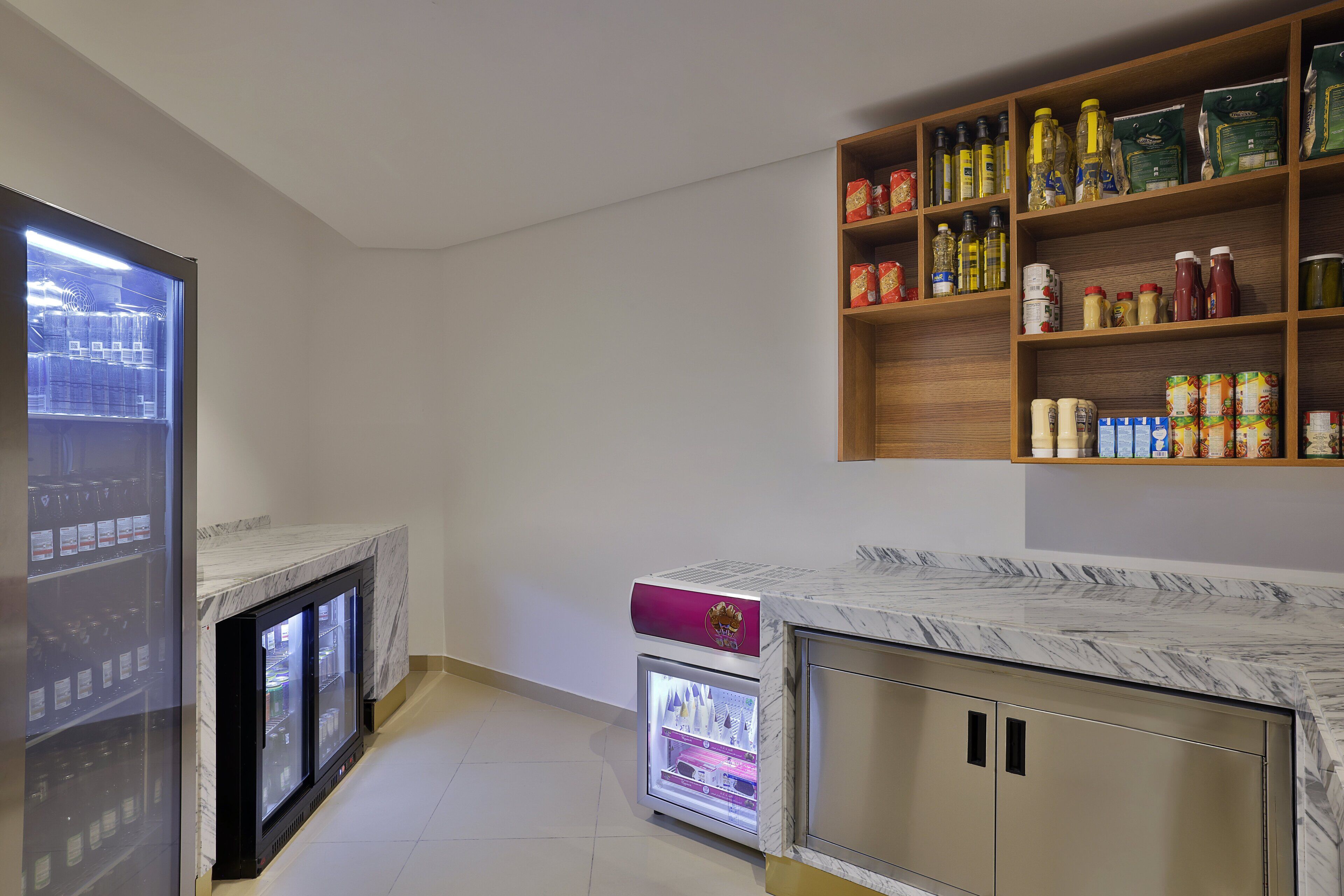 A kitchen with marble countertops, a refrigerator, and shelves stocked with various food items.