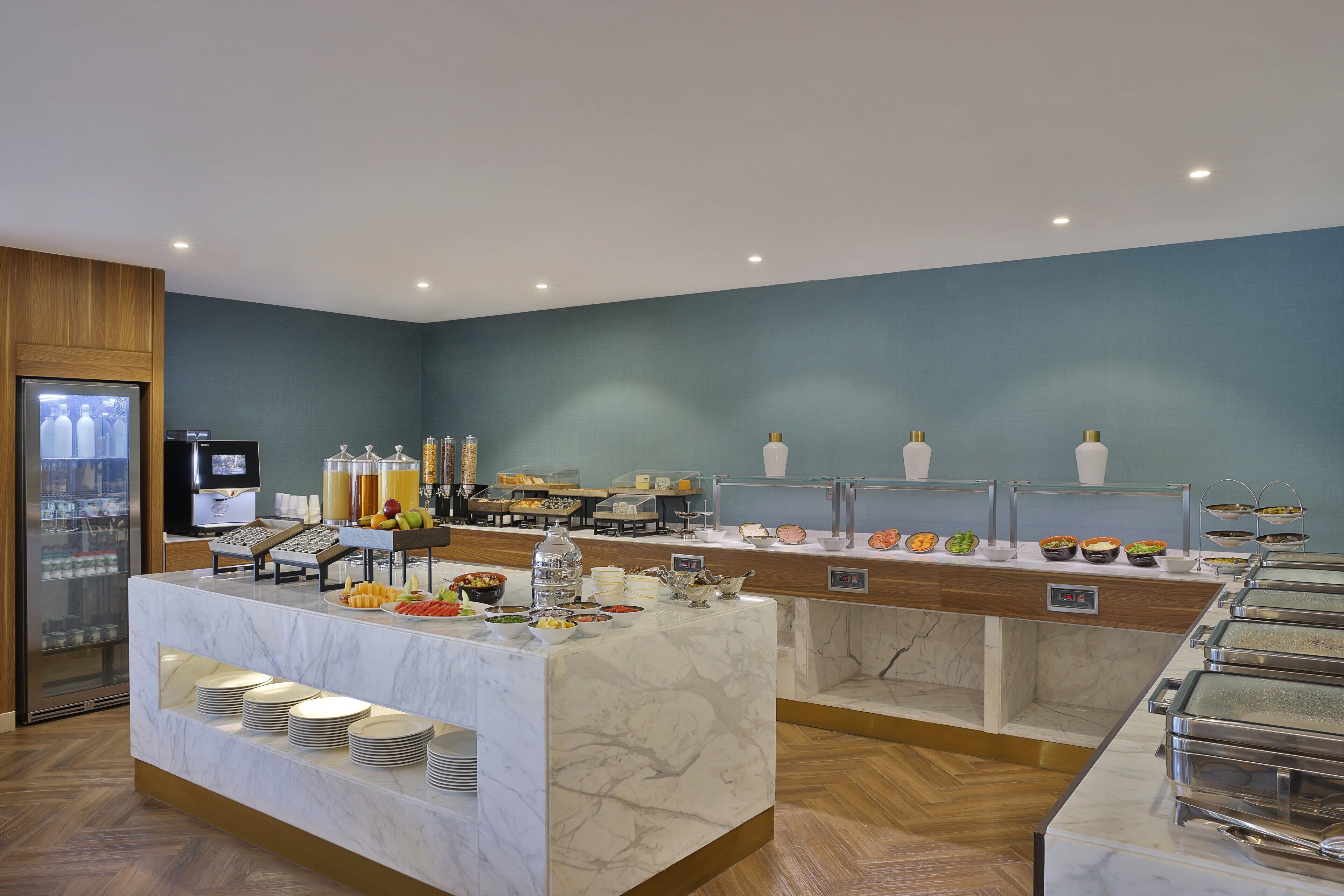 A buffet area with marble counters, a refrigerator, and various food items.