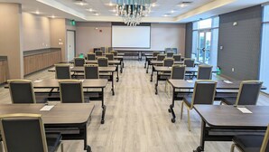 A conference room with rows of tables and chairs, a large screen, and a chandelier. - Candlewood Suites Tulsa Hills - Jenks by IHG (Jenks)