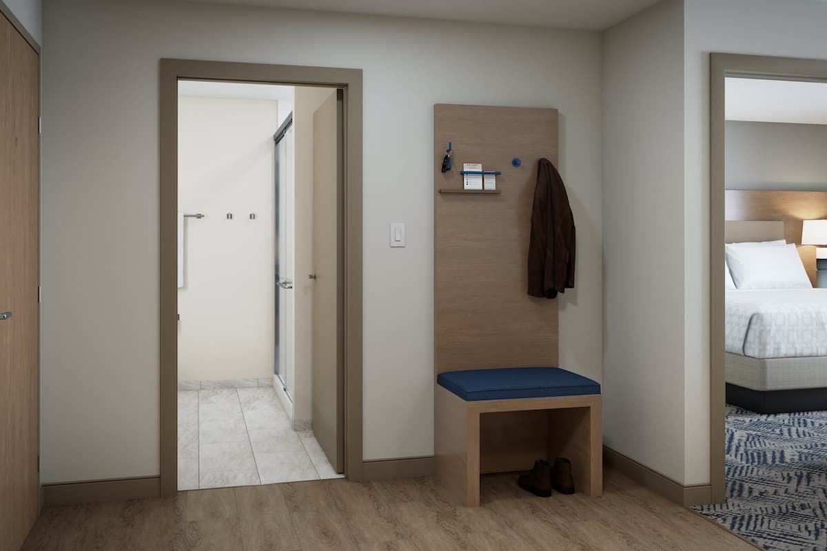 Ett hotellrum med en träbänk, en liten hylla med diverse föremål, en säng med vita sängkläder och en mönstrad matta.
