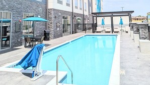 Une piscine extérieure dotée d’un espace abrité, d’un mur en pierre et de chaises longues.
