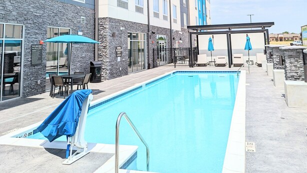 Piscina ao ar livre com área coberta, parede de pedra e espreguiçadeiras.
