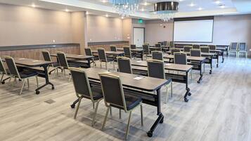 A conference room with tables and chairs, a projector screen, and a large chandelier.
