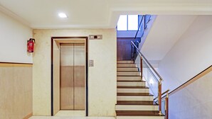 Interior com elevador de madeira, escada com corrimãos de metal e extintor de incêndio na parede.