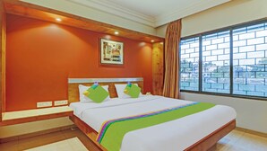 Quarto de hotel com cabeceira de madeira, uma grande janela com vista para edifícios e um quadro na parede.