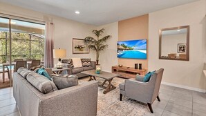 A living room with a sofa, armchair, coffee table, TV, and a plant. - Dazzling 9BR Villa with Pool& Spa, Close to Disney (Four Corners)