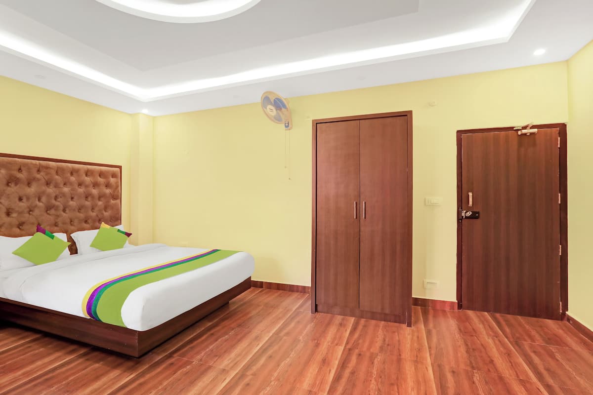 A hotel room with a tufted headboard bed, a wooden wardrobe, and a ceiling fan.