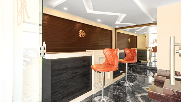 Un área de recepción con un panel de pared de madera, suelo de mármol y dos taburetes naranjas.