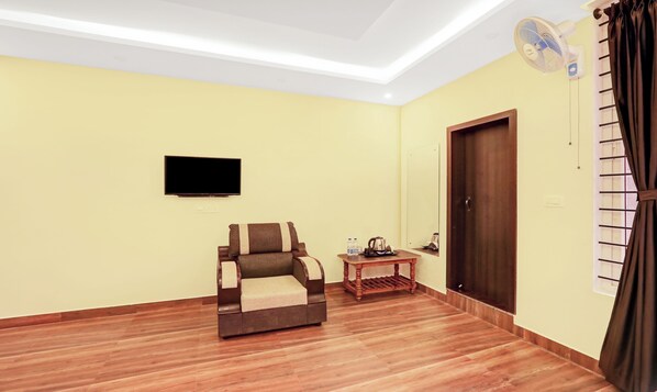 A living room with a sofa, a small table with a kettle, a flat-screen TV, and a door with a window.