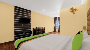 Una habitación de hotel moderna con una cama grande, un televisor de pantalla plana montado en la pared, una zona de comedor con mesa y sillas, y un ventilador de techo.