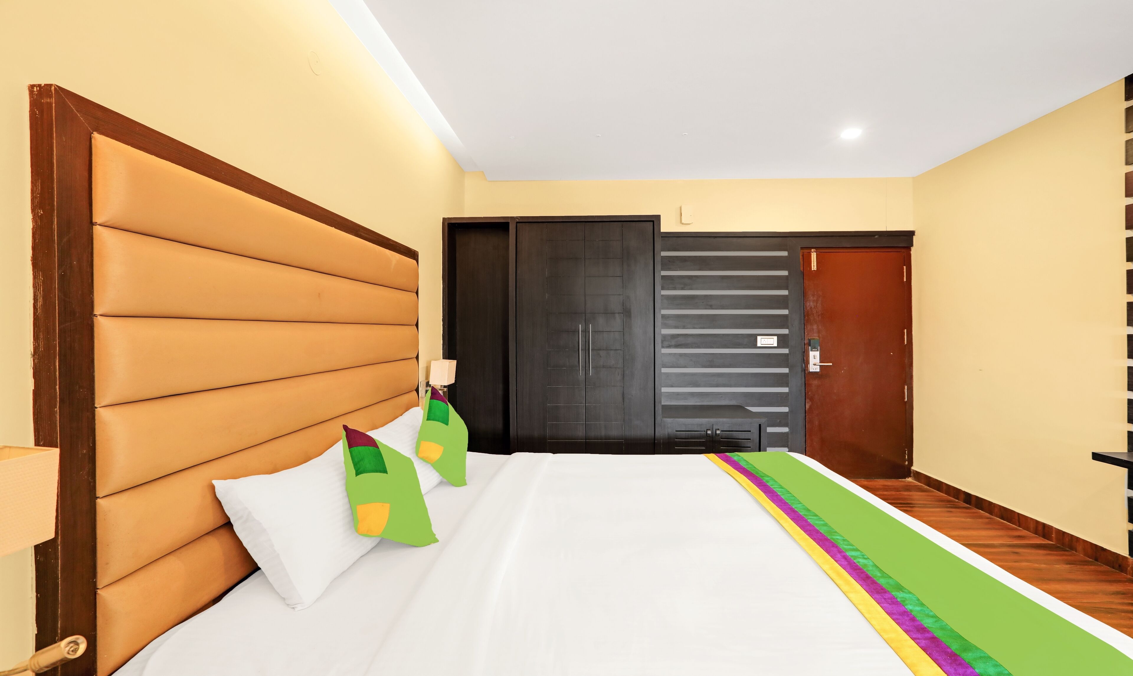 Une chambre d’hôtel avec un grand lit, une tête de lit en bois, une armoire et une porte.
