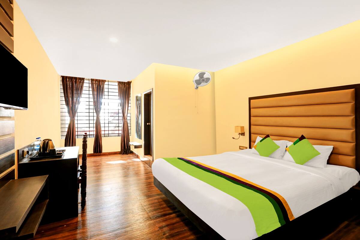 A hotel room with a large bed, a flat-screen TV, a desk with a kettle, and a window with curtains.