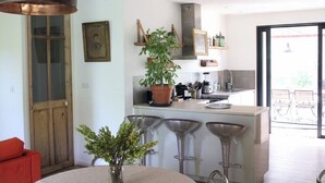 A modern kitchen with a central island, bar stools, and a large potted plant.