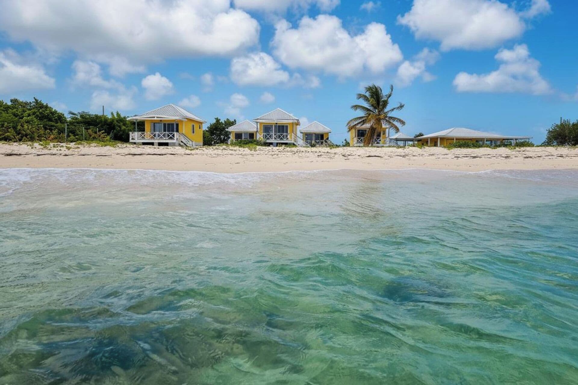 Una propiedad frente a la playa con varios edificios amarillos, aguas turquesas cristalinas y una palmera.