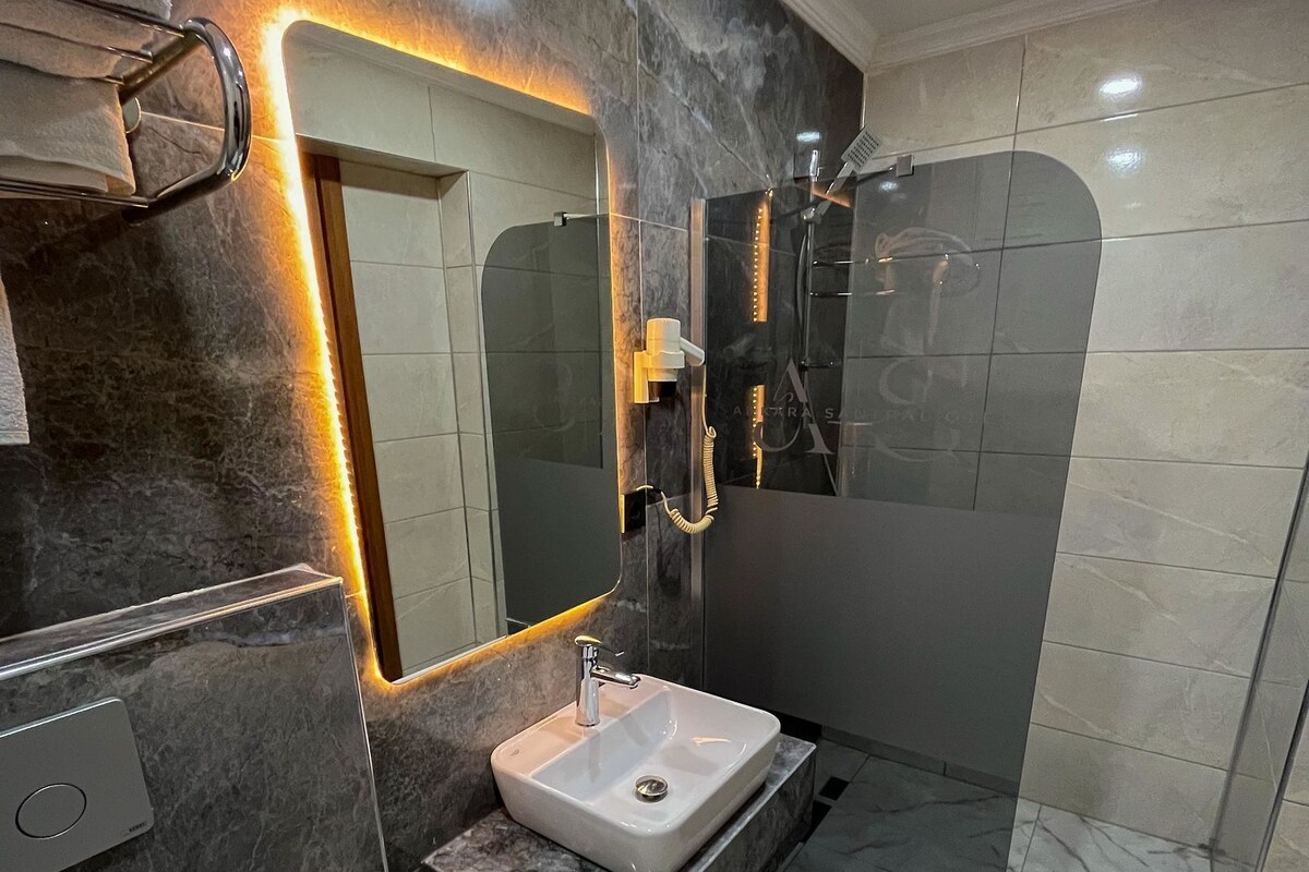 A modern bathroom with a marble sink, a large mirror, and a glass-enclosed shower.