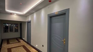Pasillo de hotel con alfombra estampada, una puerta con la inscripción 3005 y un techo moderno con iluminación empotrada.