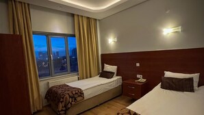 A hotel room with two beds, a window with curtains, a nightstand, and a wall-mounted light. - Ankara Santral Otel (Ankara)