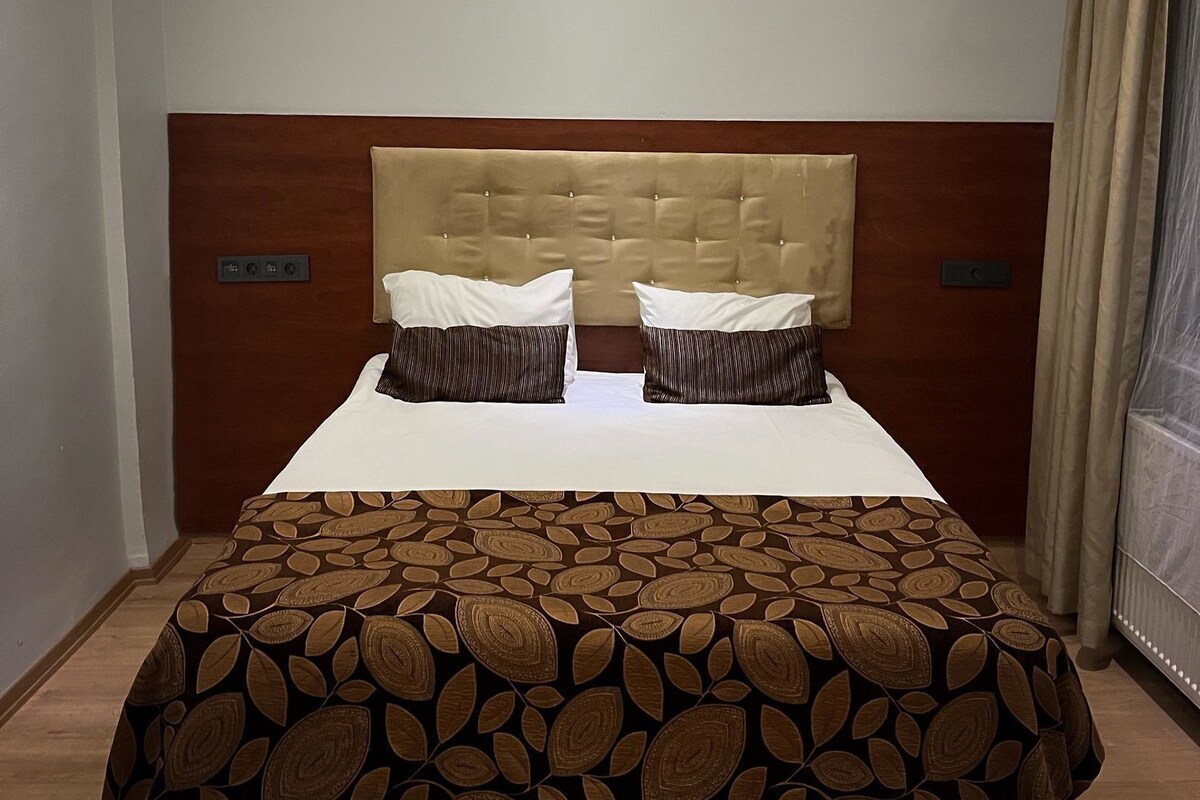 A neatly made bed with a patterned bedspread, a tufted headboard, and two pillows.