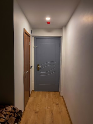 A narrow hallway with a wooden floor, a blue door with a brass handle, and a ceiling light. - Ankara Santral Otel (Ankara)