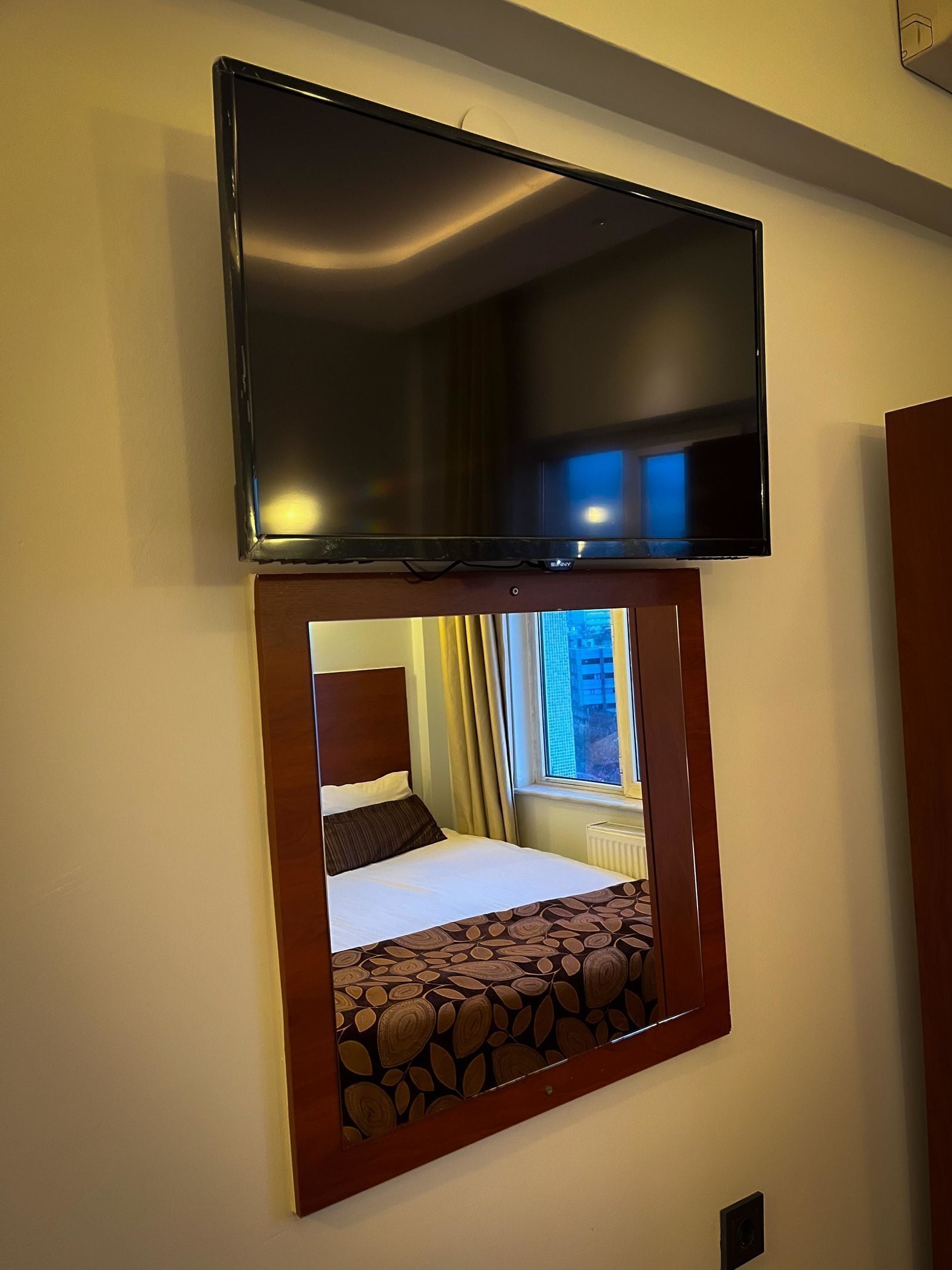 Una habitación de hotel con una cama, un televisor sobre la cama y una ventana con cortinas.