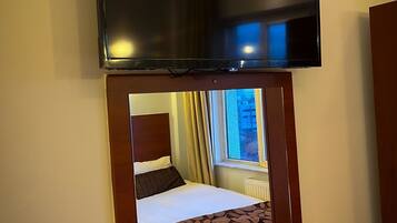 Una habitación de hotel con una cama, un televisor sobre la cama y una ventana con cortinas.