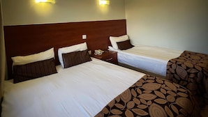 Habitación de hotel con dos camas, cada una con cabecero de madera y ropa de cama blanca. Hay dos lámparas fijadas a la pared en el techo.