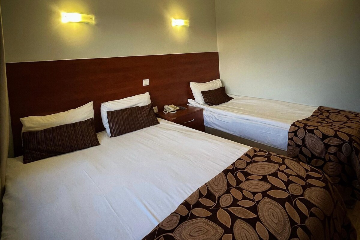 A hotel room with two beds, each with a wooden headboard and white bedding. There are two wall-mounted light fixtures on the ceiling.